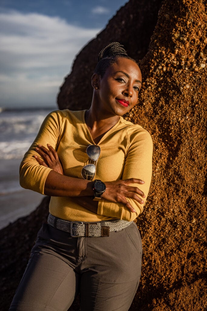 This is my signature image for The Leadership Drives — shot on location at the coast, leaning into the elements, literally. The yellow top, the aviators, the watch, the water behind me — this is what it looks like when a woman with a plan meets the road. Arms crossed not because I'm closed off, but because I've already made up my mind.