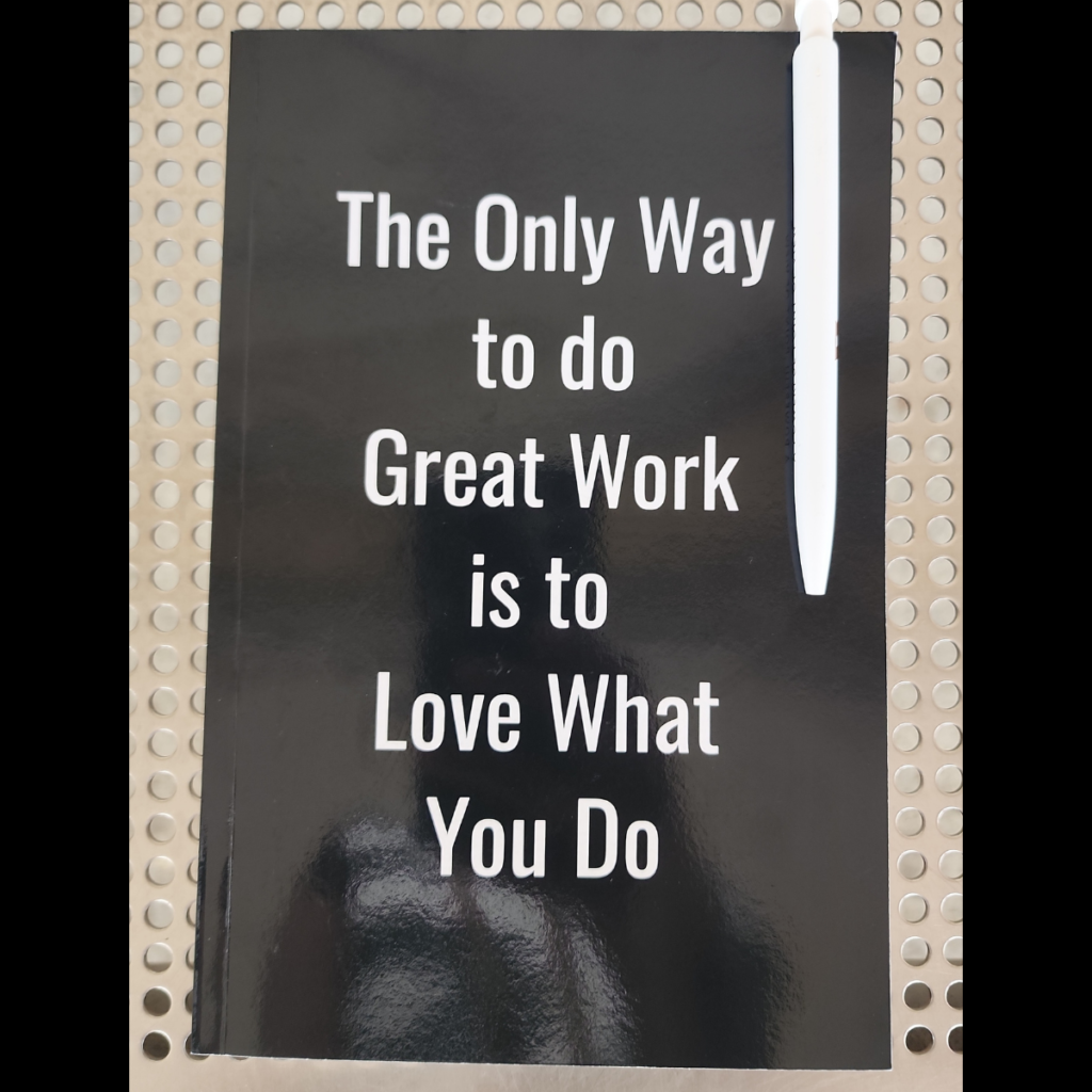 Black journal cover with white text reading "The Only Way to Do Great Work is to Love What You Do," symbolizing career fulfillment, left at 8th & Market SEPTA station in Philadelphia.